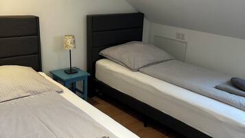 A small, cozy room with two single beds, a nightstand with a lamp, and a wooden floor.