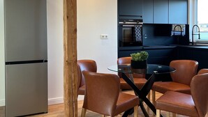 A modern kitchen with dark cabinets, a stainless steel refrigerator, and a dining area with leather chairs and a glass table. - Park View Apartment (Bremerhaven)
