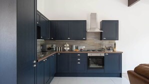 A modern kitchen with dark blue cabinets, a stainless steel range hood, and a built-in oven.