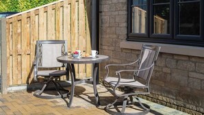 A patio with two chairs and a table, a wooden fence, and a stone wall.