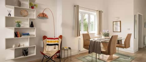 A modern living room with a dining area, wooden flooring, and a large window with curtains.