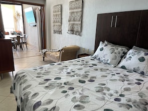 A hotel room with a large bed, a sofa, a TV mounted on the wall, and a view of the outdoor area.