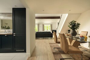A modern kitchen with dark cabinetry, a dining area with a glass table, and a view to a living room with a sofa.