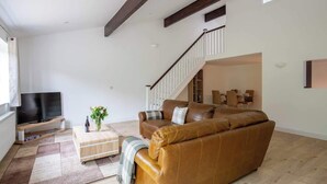 Un salon spacieux avec un canapé en cuir marron, un téléviseur à écran plat et un escalier menant à un niveau supérieur.