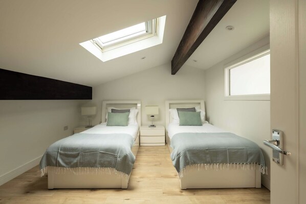 A twin bedroom with two beds, a skylight, and a wooden ceiling beam.