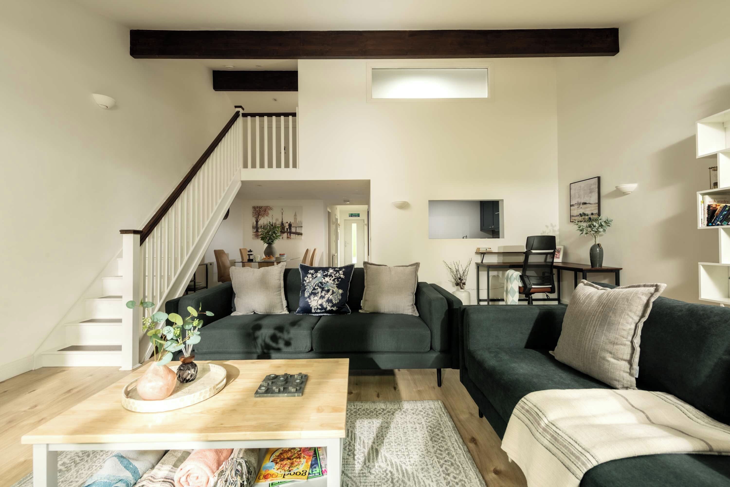 A modern living room with a staircase, a dining area, and a bookshelf.