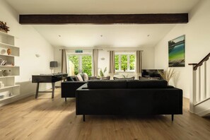 A modern living room with a sofa, a coffee table, and a bookshelf. There is a fireplace, a television, and a painting on the wall.