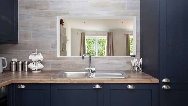Une cuisine moderne avec un grand miroir, des meubles de couleur sombre et un plan de travail en bois.