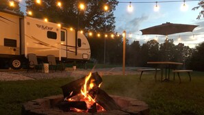 A campsite with a fire pit, string lights, and a flyte RV.