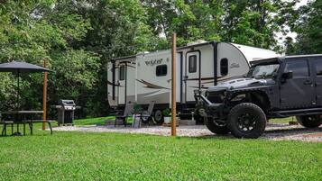 A recreational vehicle (RV) parked in a grassy area with a picnic table and grill nearby.