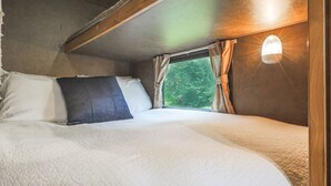 Ein gemütliches Bett mit einer weißen Decke, einem dunklen Kopfkissen und einem Fenster mit Vorhängen.