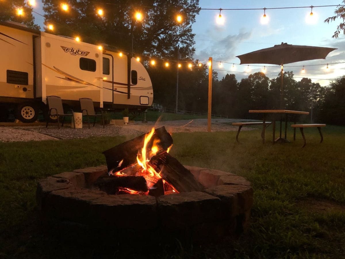 Un terrain de camping équipé d’un foyer, de guirlandes lumineuses et d’un camping-car.