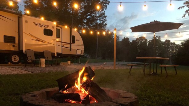 Ein Campingplatz mit Feuerstelle, Lichterketten und einem Wohnmobil von Flyte.