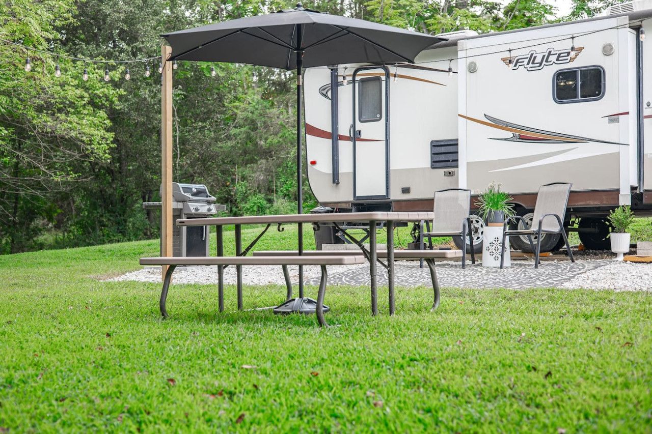 Un camping-car Flyte équipé d’une table de pique-nique et d’un barbecue, entouré de verdure.