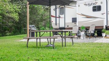 A flyte RV with a picnic table and grill, surrounded by greenery.