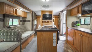 A compact RV interior with a kitchenette, a central island, a seating area, and a television.