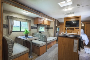 A well-equipped RV interior with a kitchenette, seating area, and a TV. - Awesome Fall Retreat- Relax After Hiking! (Harrison)