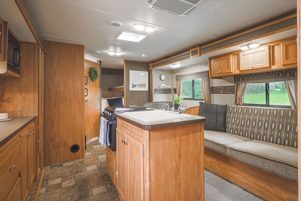 A compact RV kitchen with a central island, built-in cabinets, and a seating area with a patterned cushion.