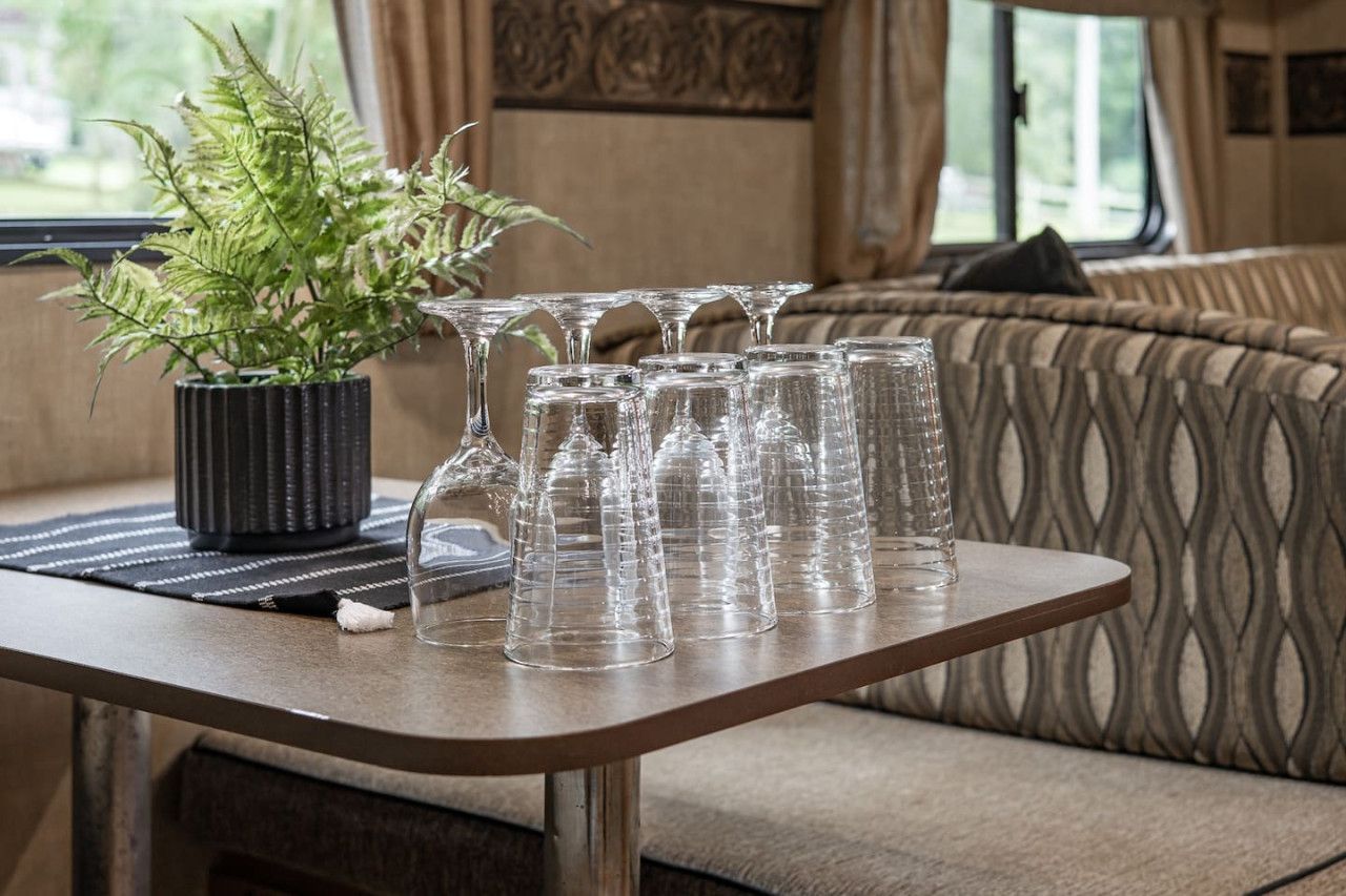 Une table sur laquelle se trouve un pot de fleurs et plusieurs verres transparents, le tout placé devant un canapé à motifs et une fenêtre avec des rideaux.