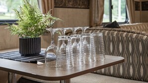 Ein Tisch mit einem Blumentopf und mehreren klaren Gläsern, vor einer gemusterten Couch und einem Fenster mit Vorhängen.