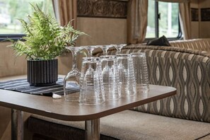 A table with a potted plant and several clear glasses, set against a patterned sofa and a window with curtains. - Awesome Fall Retreat- Relax After Hiking! (Harrison)