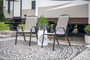 A recreational vehicle with two chairs and a potted plant on a patterned outdoor rug.