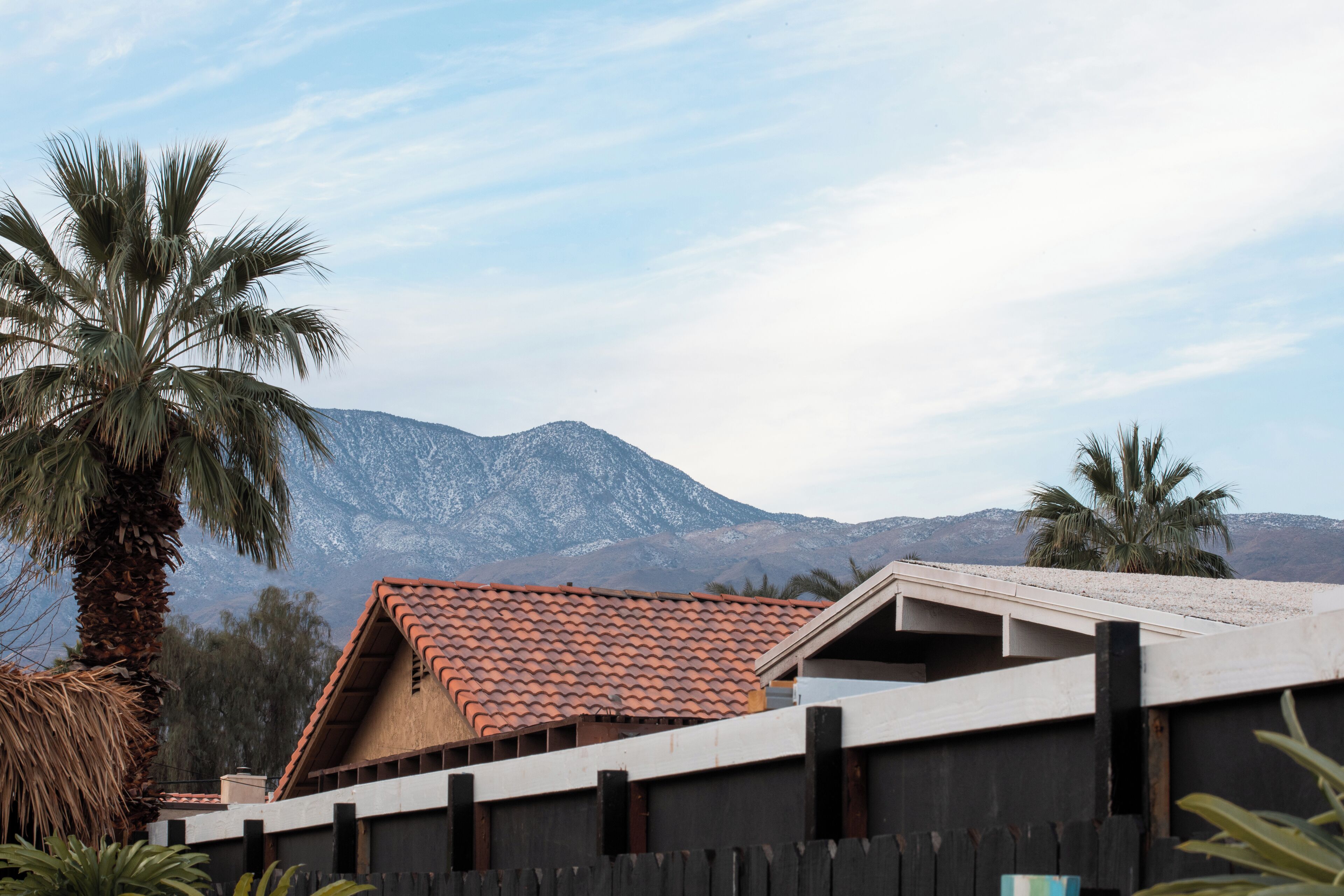 A building with a red-tiled roof, a wooden fence, and palm trees in the foreground.