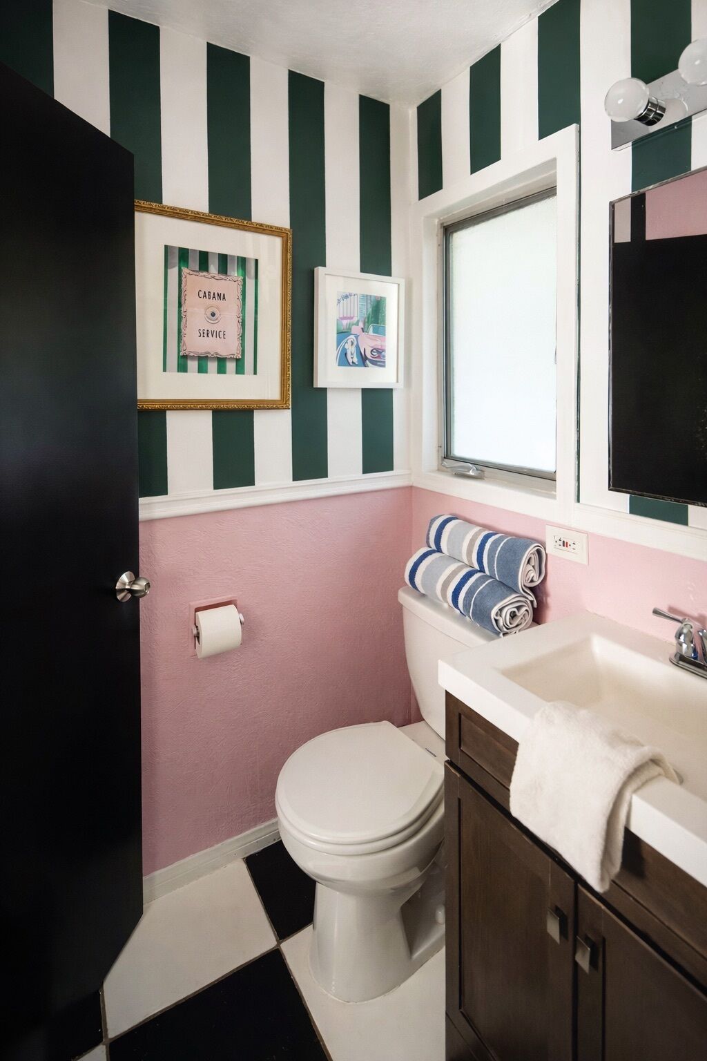 A bathroom with a toilet, sink, and towel rack. There are striped walls and a window above the sink.