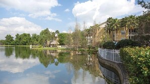 Ein friedlicher Seeblick mit Spiegelung von Himmel und Bäumen, ein hölzerner Steg und ein Gebäude mit einem Balkon mit Blick auf das Wasser.