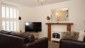 A living room with a brown leather sofa, a flat-screen TV, a fireplace, and a large mirror above it. - The Cosy Cottage Retreat! Long Stay Discounts (Llantrisant)