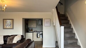A living room with a brown leather sofa, a staircase, and a kitchen in the background. - The Cosy Cottage Retreat! Long Stay Discounts (Llantrisant)