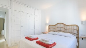 Une chambre d’hôtel avec un grand lit, des rideaux blancs, une tête de lit en bois et des serviettes soigneusement pliées.