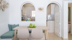 Une cuisine moderne avec des meubles blancs, une table à manger avec deux chaises et un saladier de pommes vertes posé sur la table.