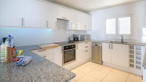 Une cuisine moderne avec des meubles blancs, un plan de travail en granit, des appareils électroménagers en acier inoxydable et une fenêtre équipée de stores.