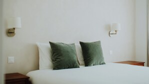 Une chambre d’hôtel avec un lit, deux oreillers verts, du linge de lit blanc et deux lampes fixées au mur.