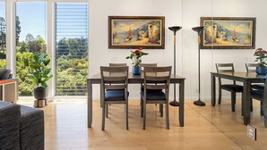 Un coin repas avec une table et des chaises, deux tableaux accrochés au mur, une plante en pot et une vue par la fenêtre.