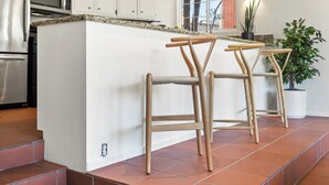 Une cuisine avec des meubles blancs, un four à micro-ondes, un ventilateur de plafond et un coin bar avec des tabourets.