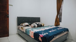Un dormitorio con cama, almohadas, una colcha, una ventana con cortinas y una puerta.