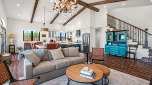 A spacious living room with a sofa, coffee table, and a dining area with chairs and a table. A kitchen with modern appliances and a staircase with a railing is visible in the background. - Luxe Healdsburg 3BR Home + Comp Ridge Wine Tasting (Healdsburg)