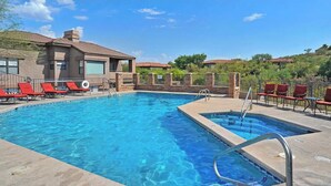 A rectangular swimming pool with clear blue water, surrounded by red lounge chairs and a stone wall.