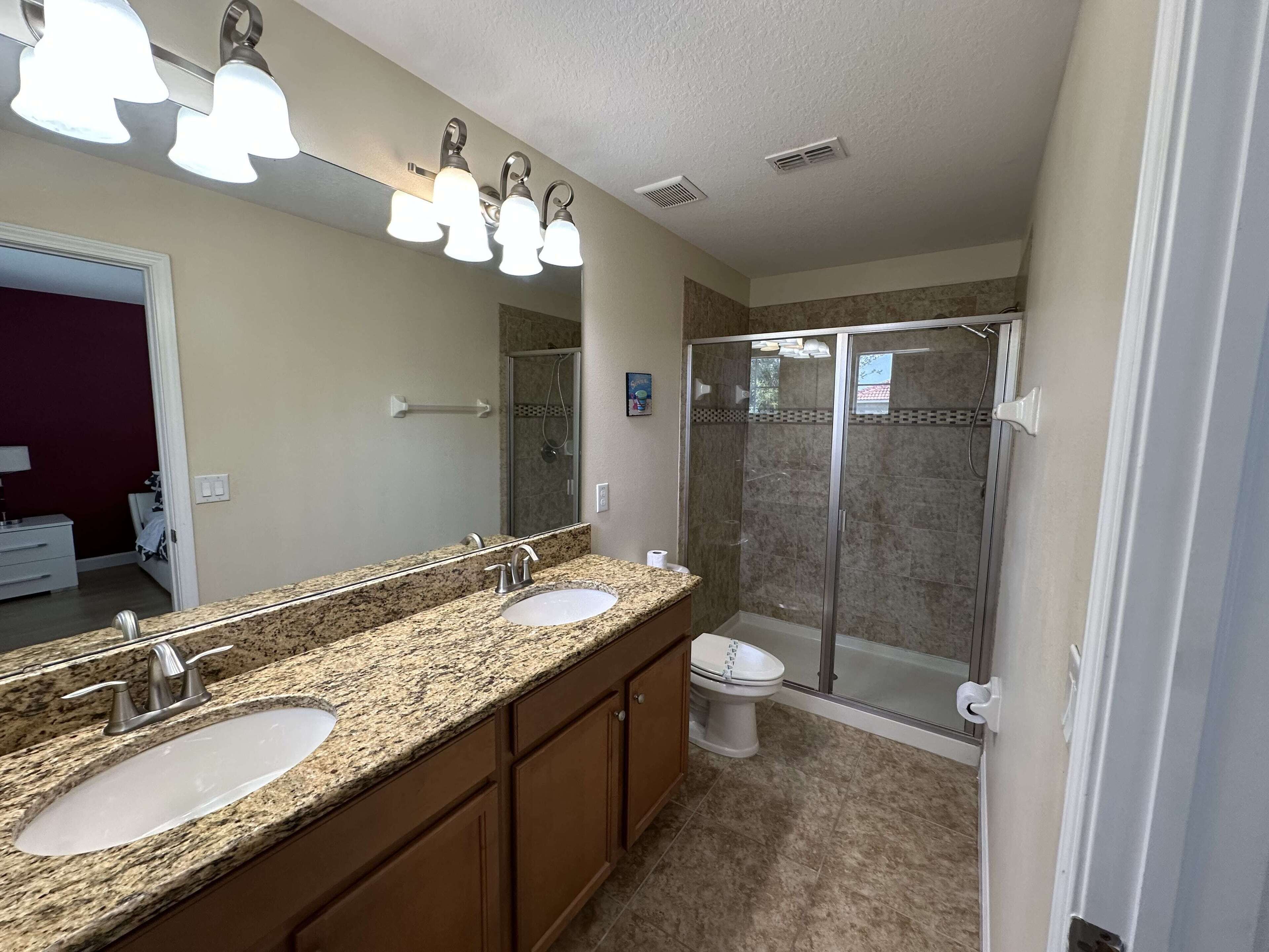 A bathroom with a double sink, a large mirror, a shower enclosure, and a toilet.