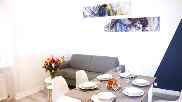 A dining area with a table set for four, a grey sofa, and abstract art on the wall.