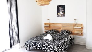A bedroom with a zebra-patterned bedspread, a wooden slatted headboard, a woven rattan pendant light, and a zebra-themed painting on the wall.