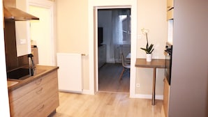 A modern kitchen with a built-in oven, a stainless steel range hood, and a wooden countertop. There is a potted plant on the countertop and a chair in the background.