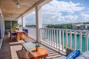 A balcony with a wooden table, blue chairs, and a view of a body of water. - Relaxing Waterfront Getaway in Puerto Aventuras (Puerto Aventuras)