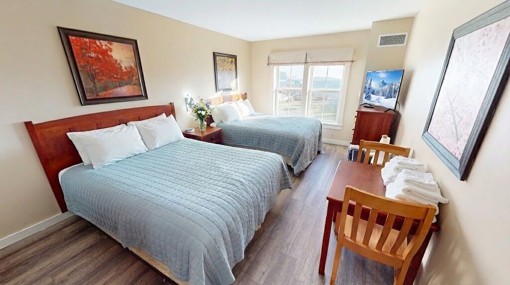 A hotel room with two beds, a wooden table with chairs, a TV, and framed artwork on the walls.