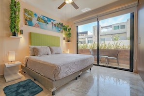 A bedroom with a bed, a green headboard, a painting, and a view through a sliding door.