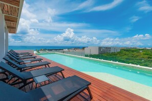 A rooftop pool with lounge chairs and a clear view of the ocean.