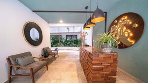 A modern lobby with a wooden reception desk, a sofa, and a circular mirror. - Studio Caribbean Dreams (Playa del Carmen)