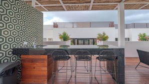 An outdoor bar area with a wooden bench, a trash bin, and a patterned wall. - Studio Caribbean Dreams (Playa del Carmen)